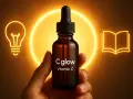 En hand håller en flaska Cglow Vitamin C. En glödlampa och en öppen bok lyser upp bakgrunden. Perfekt för att lära sig om att dricka askorbinsyra.