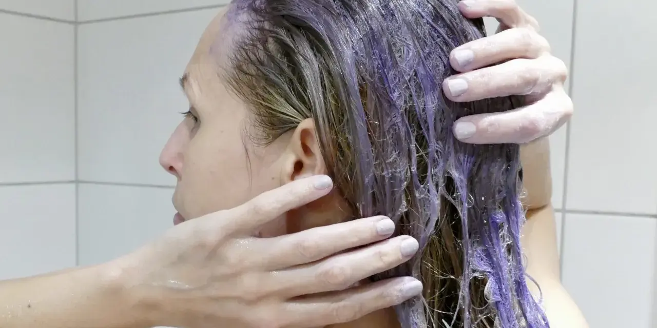 En person masserar in silverschampo med blå pigment i sitt blonda hår.