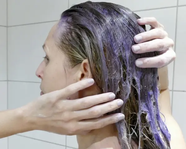 En person masserar in silverschampo med blå pigment i sitt blonda hår.