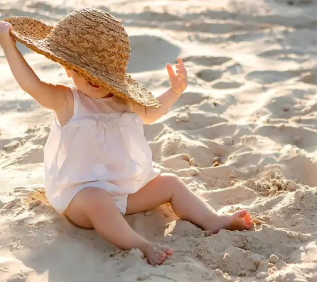 Liten bebis med stråhatt på stranden, njuter av solens värme.