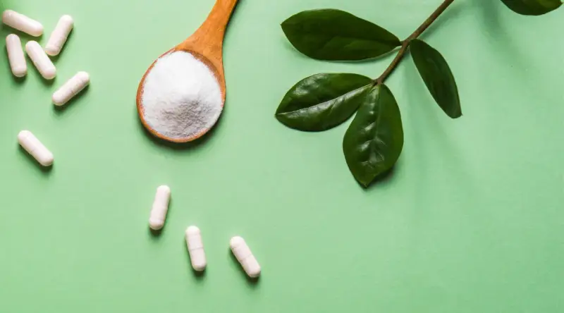 Vita C-vitaminer i kapslar och pulver på en sked, med gröna blad.