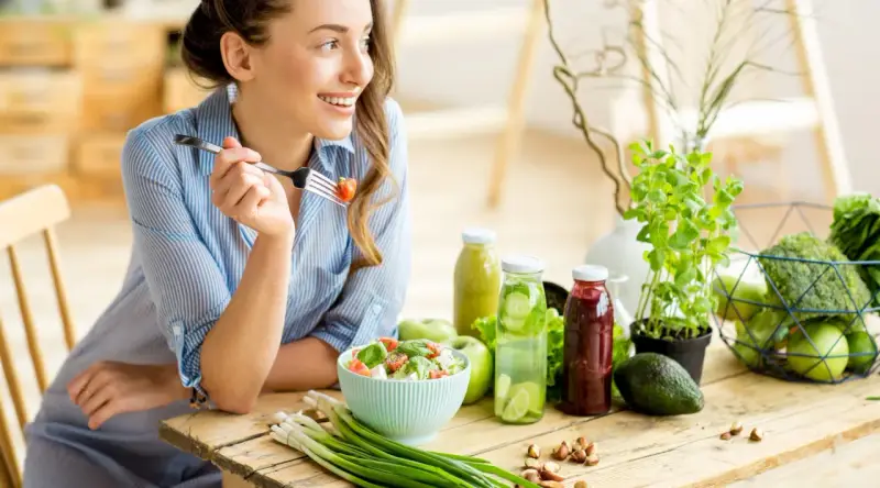 Kvinna äter sallad, omgiven av hälsosam mat. Kan vara en del av en kost för att undvika brist på kisel symtom.