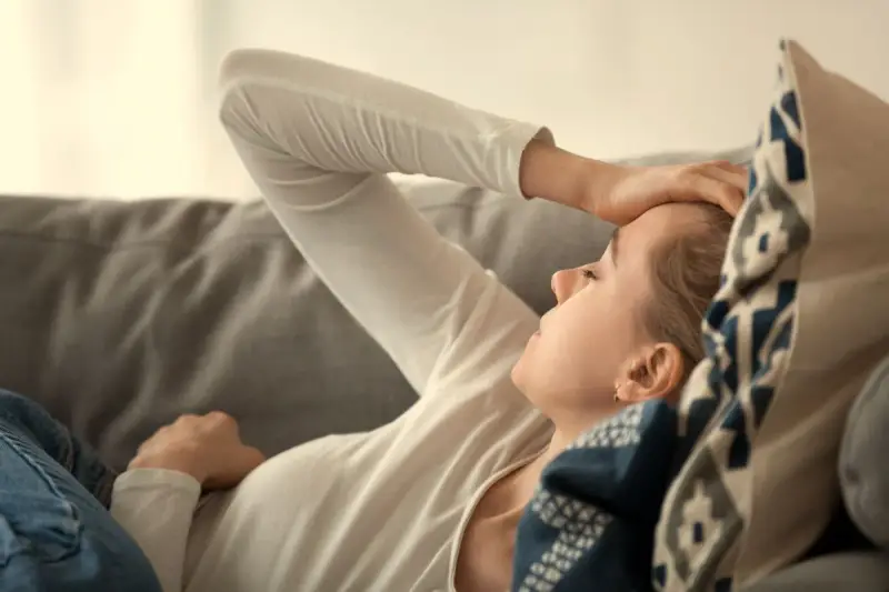 En kvinna med handen mot pannan, utmattad. Kan vara tecken på b12-brist stress.